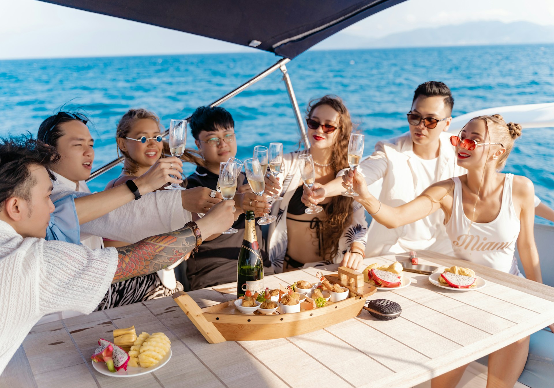 Guests raising champagne glasses over a chef's spread on a yacht deck